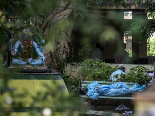 BBC Mundo: Un hombre vestido en traje protector descansa en un banco antes de realizar los ritos fúnebres a un familiar víctima de covid-19, en Bombay. 13 de abril de 2021