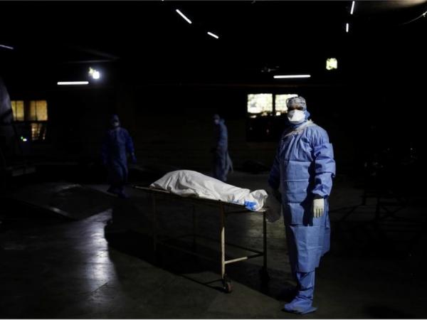 BBC Mundo: Un trabajador de la salud, vestido en traje de protección personal, espera frente al cuerpo de un hombre que murió de covid-19, antes de su cremación en Nueva Delhi, India, 21 de abril de 2021